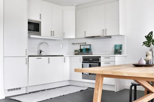 a kitchen with white cabinets and a wooden table at Mysigt hus med kamin och pool in Torekov