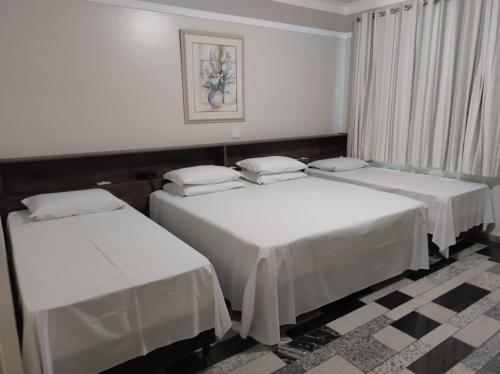 two beds in a room with white sheets at Lodi Express Hotel in Arapongas