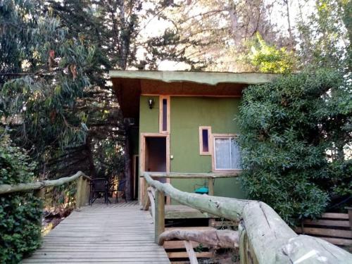 una casa verde con una pasarela de madera que conduce a ella en cabaña rustica LEMU isla negra, en Isla Negra