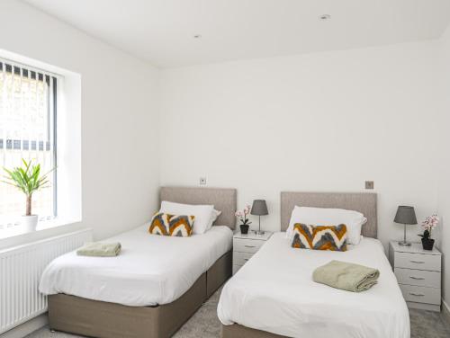 two beds in a bedroom with white walls and a window at Bryn Min Manton Apartment in Caernarfon