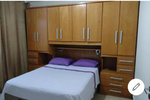 Schlafzimmer mit einem Bett mit lila Kissen und Holzschränken in der Unterkunft Apto São Bernardo do Campo 33 in São Bernardo do Campo