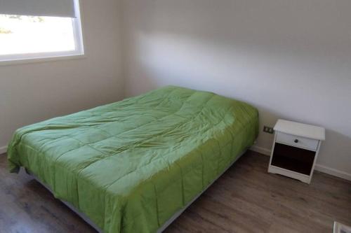 1 dormitorio con cama verde y mesa pequeña en Comfortable and quiet apartment. Pelluco Alto, en Puerto Montt