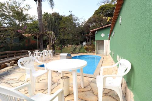 um pátio com cadeiras brancas, uma mesa e uma piscina em Pousada Maria Bonita em Macacos