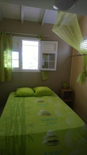 a bedroom with a green bed with a window at Zénitude Bungalow in Le Lorrain