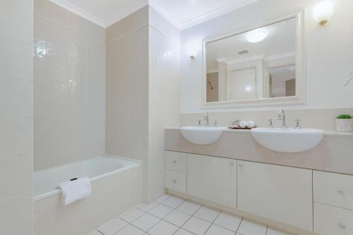 a bathroom with two sinks and a tub and a mirror at The Lakes Resort Cairns in Cairns