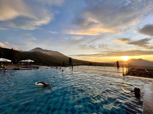 a person swimming in a swimming pool with the sunset in the background at Alinson Sunset Hill in Bogor
