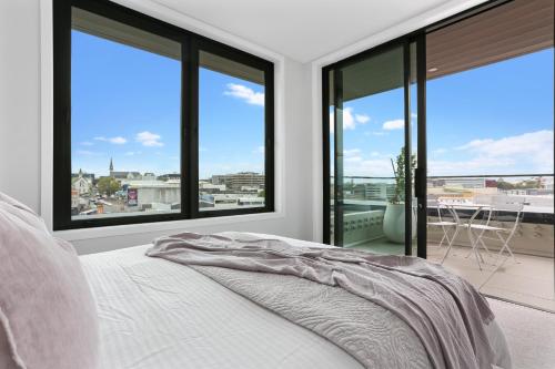 een slaapkamer met grote ramen en een bed met een deken bij Enfield Sky - Brand New Luxury Penthouse in Auckland