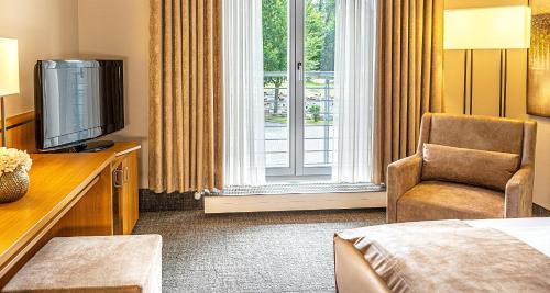 una camera d'albergo con letto, TV e sedia di Victor's Residenz-Hotel Teistungenburg a Teistungen