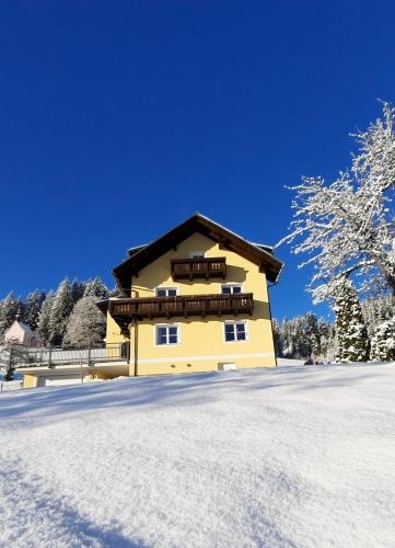 a yellow house in the snow with trees in the background at Kalvarienberg Appartement Gosau in Gosau