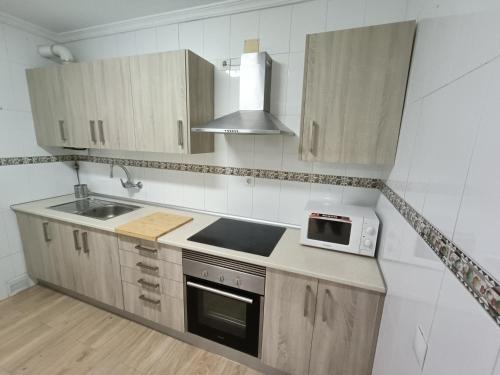 a kitchen with wooden cabinets and a sink and a microwave at Piso Avenida junto a la Playa in Cádiz