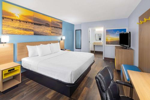 a hotel room with a bed and a desk and a television at Days Inn by Wyndham Pensacola I-10 in Pensacola
