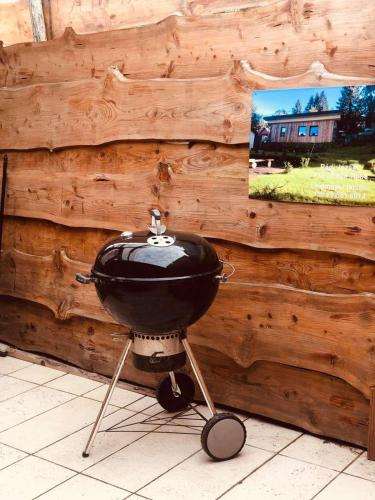 a grill on a stand in front of a wooden wall at Larix Mátra Vendégház in Matraszentlaszlo