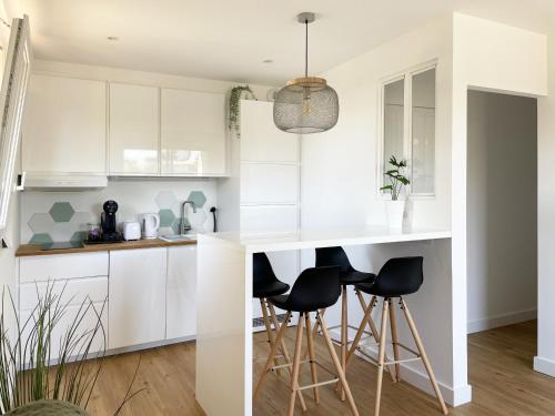 a kitchen with white cabinets and black bar stools at Au pied des dunes in Seignosse