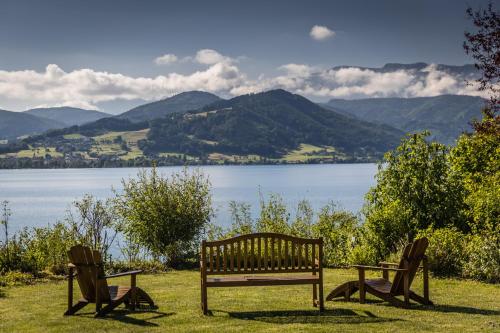 a bench and two chairs in front of a lake at Villa Weiss in Attersee am Attersee