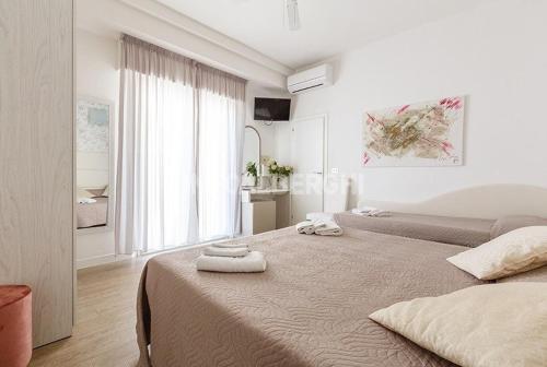 a white bedroom with two beds and a window at Hotel Ermeti B&B Brunch in Riccione