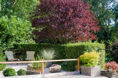 a garden with two chairs and a tree with red flowers at Au Grand Fête, B&B à la campagne in Le Fête