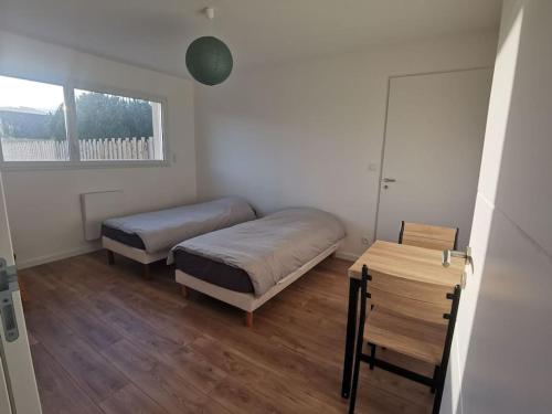 1 Schlafzimmer mit 2 Betten, einem Tisch und einem Fenster in der Unterkunft Maison neuve au calme à 2 pas du Mans et des 24h. in Ruaudin