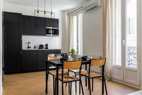 une cuisine avec des armoires noires, une table et des chaises dans l'établissement IMHOST - Appartement luxueux climatisé -Marseille -Le Panier, à Marseille