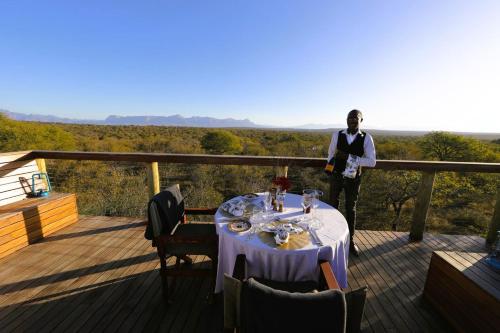 a man standing on a deck with a table on a balcony at Oase by 7 Star Lodges - Greater Kruger Private 530ha Reserve in Hoedspruit