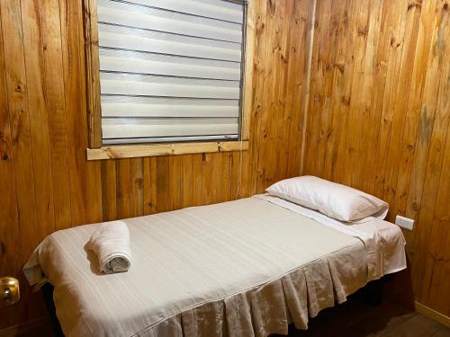 a bed in a wooden room with a window at Cabañas Puerto Aysen in Puerto Aisén