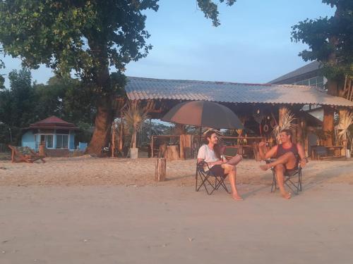 two people sitting in chairs under an umbrella on the beach at Miss You Beach Resort Koh Mak in Ko Mak
