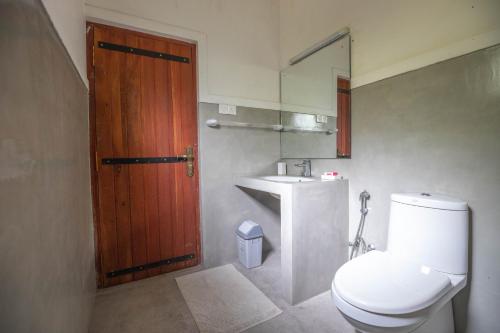 baño con aseo y lavabo y puerta de madera en Kuru Ganga Villa, en Eratnagoda