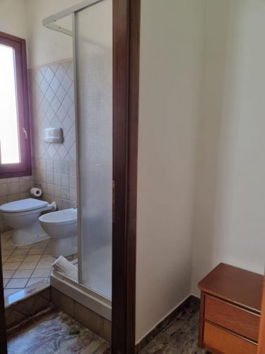a bathroom with a toilet and a glass shower door at Hotel Plammas in Santa Maria Navarrese