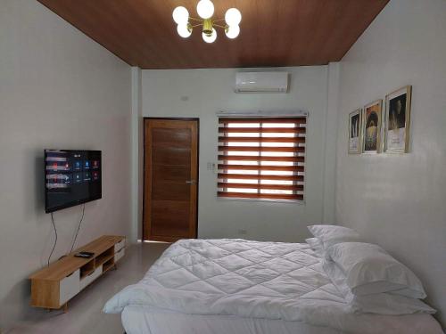 Un dormitorio blanco con una cama y un televisor. en FLB Apartelle Los Banos, en Los Baños