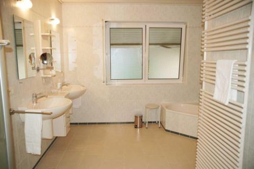 een badkamer met 2 wastafels, een bad en een raam bij Ferienwohnung 8 in Ochsenhausen