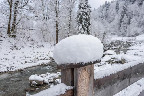 a wooden post covered in snow next to a river at Schwüwong - Apartment 03 in Kelchsau