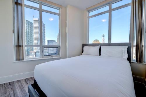 una camera da letto con un grande letto bianco e due finestre di Grand Royal condos SQ One Mississauga a Mississauga