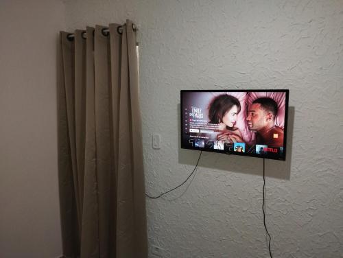 PRAIA ENSEADA - WI-FI e AR CONDICIONADO في غوارويا: تلفزيون بشاشة مسطحة معلق على جدار بجوار ستارة
