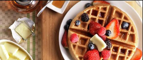 a plate of waffles with fruit on a table at Home2 Suites By Hilton Dallas Medical District Lovefield, Tx in Dallas