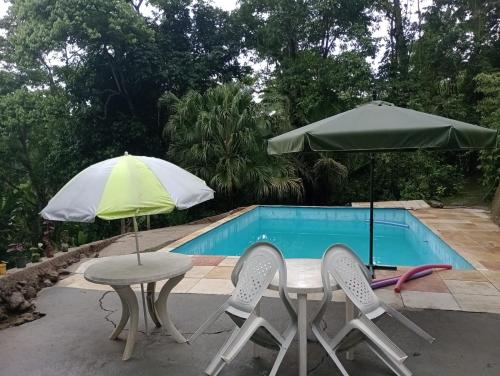 dos sombrillas, una mesa y sillas junto a una piscina en Suítes Caminho das Rosas Experiência na Montanha en Guapimirim