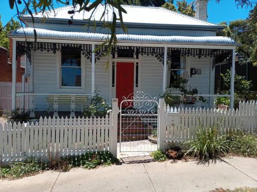 a white fence in front of a house with a red door at The Artist's Cottage in Bendigo