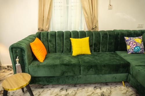a green couch with three yellow pillows on it at Discover 8-Bedrooms Lakeside Apartment Living Free Starlink SuperFast Speed WiFi And Well Secured in Amuwo