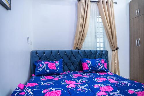 a blue bed with pink and purple pillows and a window at Discover 8-Bedrooms Lakeside Apartment Living Free Starlink SuperFast Speed WiFi And Well Secured in Amuwo
