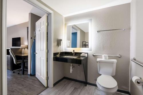 a bathroom with a toilet and a sink and a desk at SureStay Hotel by Best Western Spring North Houston in Spring