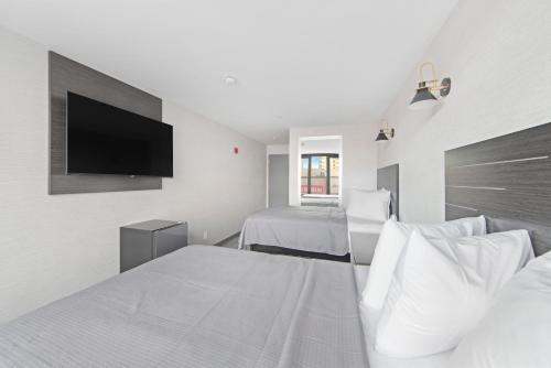 a white bedroom with two beds and a flat screen tv at Hotel TREMONT Bronx Yankee Stadium in Bronx