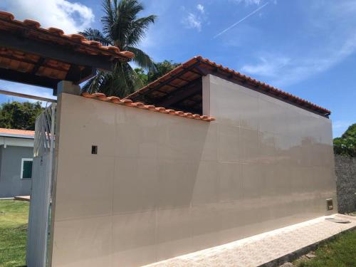 a white wall next to a house with a palm tree at Casa de praia em Barra do Gil in Vera Cruz de Itaparica