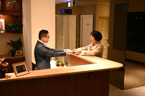 a man and a woman shaking hands at a counter at Lütel Hotel Xpark Gloria Outlets Shin Kong Cinemas in Dayuan