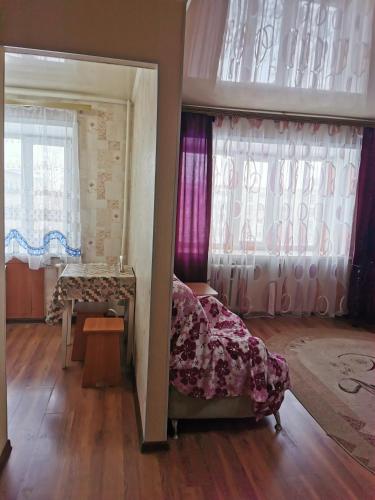 Cette chambre comprend un lit, une table et des fenêtres. dans l'établissement 1 комн апартаменты в центре рядом с парком, à Kostanay