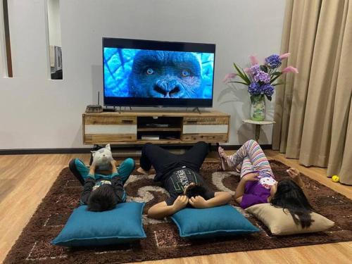 drie kinderen liggen op kussens voor een tv bij Inap@Rusa in Bachok