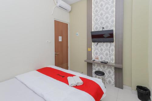 a bedroom with a bed with a red blanket and a tv at RedDoorz at Ngaggel Jaya Surabaya in Surabaya
