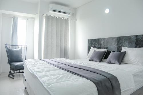 - une chambre blanche avec un grand lit et une chaise dans l'établissement Kia Servised Apartmen at Grand Sentraland Karawang, à Karawang
