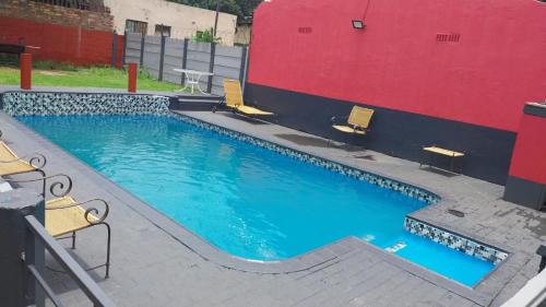 een groot zwembad met stoelen naast een rode muur bij Jay's Guest House in Witbank