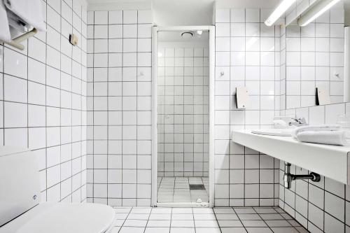 a white tiled bathroom with a shower and a toilet at Best Western Plus Hotel Bakeriet in Trondheim