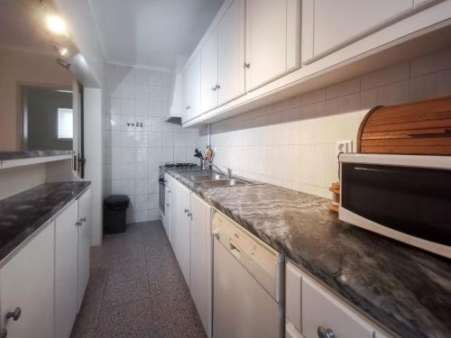 a kitchen with white cabinets and a sink and a microwave at Brisa apart t2 in Ovar