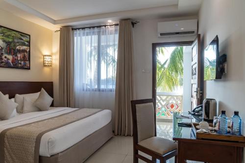 a hotel room with a bed and a desk and a window at PrideInn Hotel Diani in Diani Beach