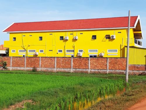 a yellow building with a red roof next to a field at Ban Sokluy AC apartment 3 1-2pax including kitchen in Siem Reap